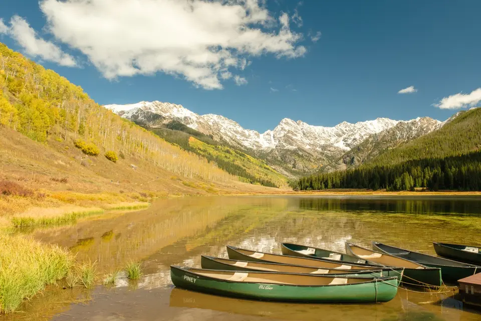 Canoes on the shore of an alpine lake below snowy peaks in fall