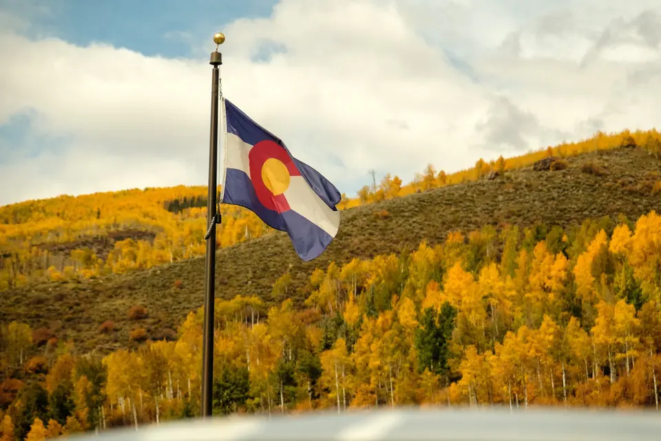 Colorado state flag flying above golden aspens